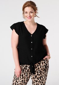 Blouse noire à col en V avec texture en dentelle, manches courtes à volants et détails en boutons argentés. Porte avec un pantalon à imprimé léopard.
