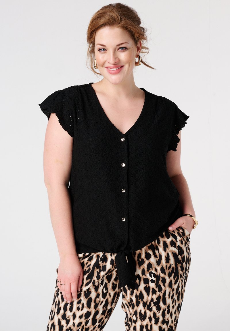 Blouse noire à col en V avec texture en dentelle, manches courtes à volants et détails en boutons argentés. Porte avec un pantalon à imprimé léopard.