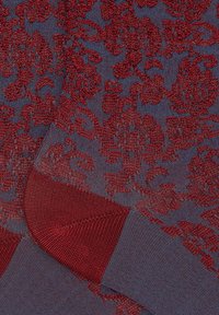 Motivo floreale rosso su un tessuto di maglia blu, con una consistenza liscia e dettagli a polsino a coste. Gli accenti includono sottili variazioni nella tessitura.