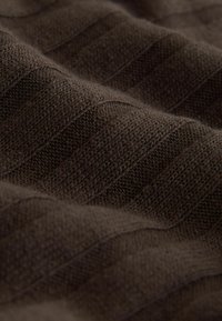 Prim-plan al unei țesături tricotate maro, texturată, care prezintă un model ondulat, evidențiind fibrele moi și detaliile intricate ale designului.