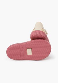 Beige slip-on shoes with a pink rubber sole. Features a textured pattern on the sole and a small logo. Material appears smooth and durable.