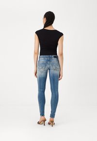 Tajta blå jeans med ett bleknat mönster på benen, fem fickor och en svart midja. Bärs med en svart topp och klacksandaler.