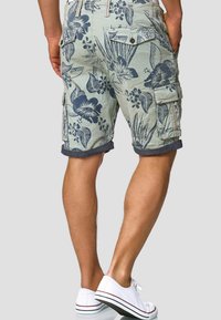 Shorts cargo en tissu vert clair avec un imprimé floral bleu marine, ourlet roulé, poches latérales et coupe décontractée. Associés à des baskets blanches.