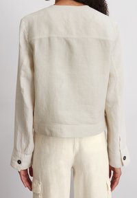 Beige linnedjakke med rund hals, cropped design og lange ærmer med knaplukninger ved manchetterne. Glat tekstur.