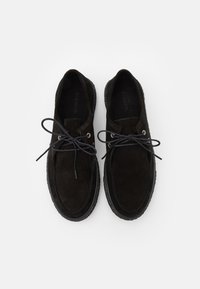 Scarpe in suede nero con punta tonda, allacciatura frontale e suola in gomma nera a contrasto. Presentano occhielli in argento e soletta testurizzata.