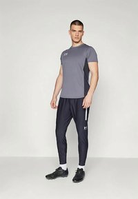 Siva kratka športna majica s kratkimi rokavi z logotipi, v kombinaciji z mornarsko modrimi ožjimi trenirčkami z belim stranskim pasom in črnimi športnimi copati.