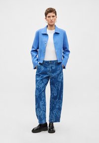 Μπλε υφασμάτινο κοντό σακάκι, λευκό πουκάμισο και φαρδιά τζιν παντελόνια με παγιέτα μοτίβο. Μαύρα χοντρά παπούτσια ολοκληρώνουν το σύνολο.