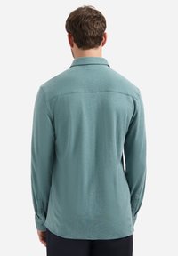 Langarmshirt van lichtteal stof, met een kraag en knoopmanchetten. Glad materiaal met een iets relaxte pasvorm en een detail op de achterkant.