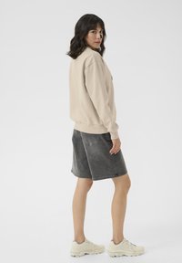 Beige sweatshirt with ribbed cuffs, paired with dark gray shorts. Cream sneakers with textured detailing complete the outfit.
