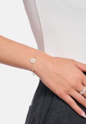 Silberfarbene Armbanduhr mit floralem Design, zentralem gelbem Edelstein und zartem Kettchen, getragen an einem Handgelenk vor hellem Hintergrund.