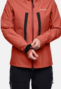 Rode waterdichte jas met zwarte accenten, voorzien van een ritssluiting aan de voorkant, twee borstzakken en verstelbare manchetten voor een veilige pasvorm. Gemaakt van Ceplex Pro-materiaal.
