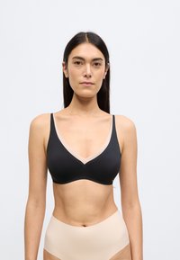 Μαύρο ασύρματο σουτιέν με ντεκολτέ σε σχήμα V, με γυμνό διακοσμητικό κατά μήκος των άκρων. Ομαλό ύφασμα και μινιμαλιστικός σχεδιασμός.
