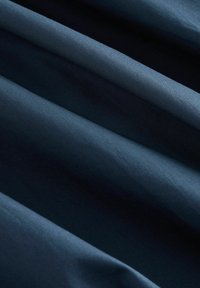 Tissu bleu foncé avec une texture lisse, affichant de subtiles ondulations et plis, illustrant ses qualités légères et drapées.