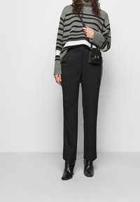 Szary i czarny sweter w paski z prążkowanymi mankietami, zestawiony z teksturowanymi czarnymi spodniami. Modelka trzyma małą czarną torebkę i ma na sobie czarne botki za kostkę.