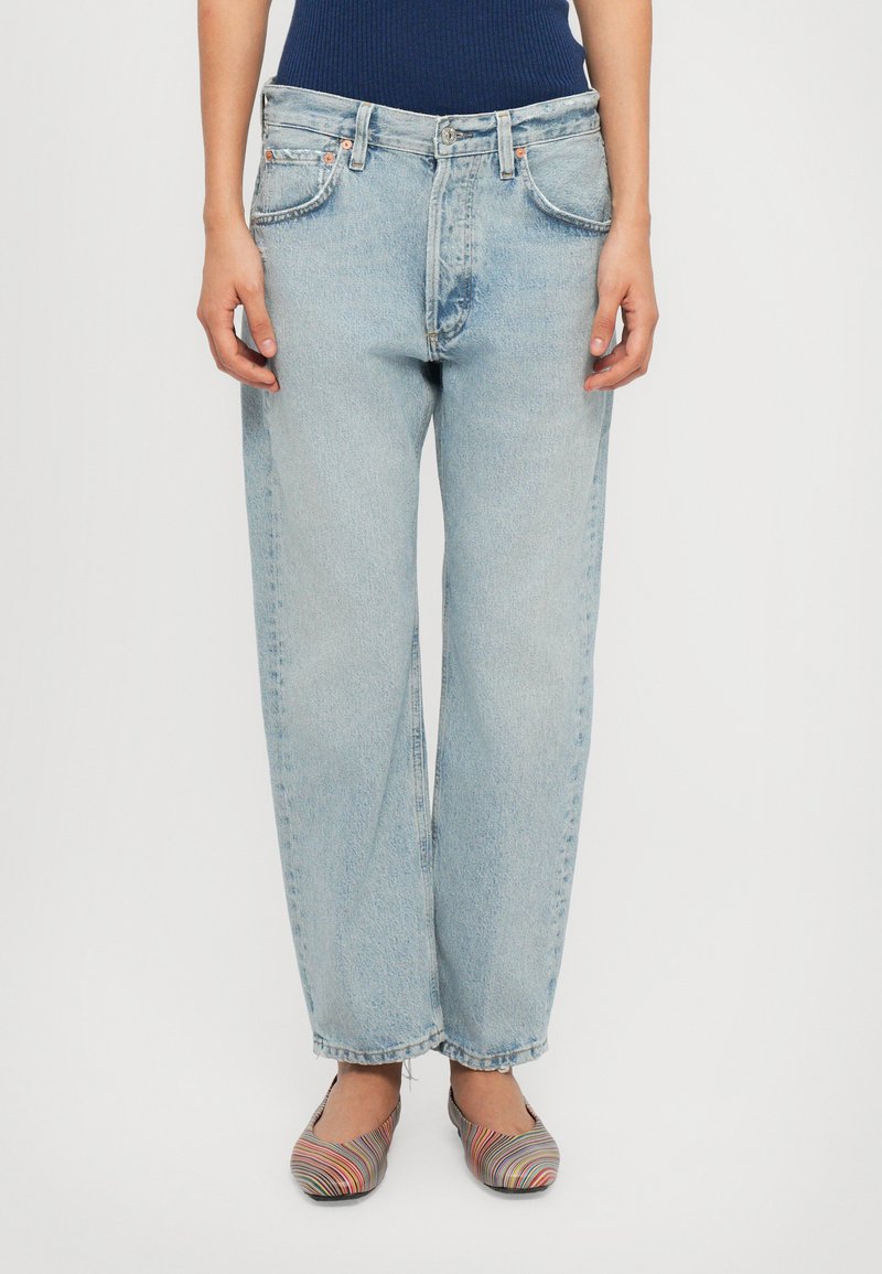 Light blue, high-waisted jeans with a straight fit. Features five pockets, faded texture, and copper-tone hardware. Worn with striped flats.