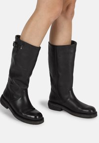 Bottes noires en cuir, montant jusqu'au genou, avec une finition lisse, bout arrondi et talon carré. Comprend une sangle décorative avec une boucle en accent au sommet.