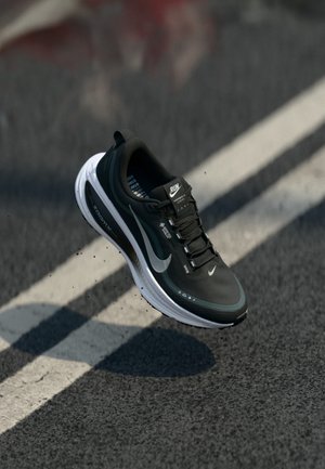Sapatilha atlética preta com parte superior em malha, sola branca, detalhes refletivos e atacadores pretos. Apresenta a marca Nike e um design acolchoado.