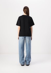 Black cotton t-shirt with a relaxed fit, short sleeves, and a rounded neckline, paired with light blue wide-leg jeans.