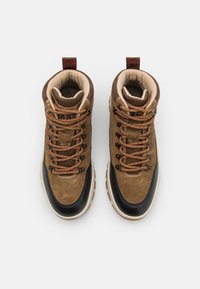 Brązowe zamszowe buty trekkingowe z czarnym gumowym czubkiem, jasnobrązowymi sznurowadłami i wyściełanym kołnierzem. Posiadają pętelkę na zapięcie oraz teksturowaną podeszwę dla lepszej przyczepności.