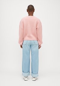 Gaišs rozā lielizmēra džemperis ar nokritušām plecu daļām un ribotu apakšmalu, apvienots ar gaiši zilajiem platajiem džinsiem, ar sarullētām piedurknēm un baltām sporta kurpēm.