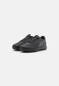 Chaussures de sport noires avec une tige synthétique lisse, des accents texturés et une semelle extérieure robuste pour une bonne adhérence. Équipées de lacets noirs et d'un logo.