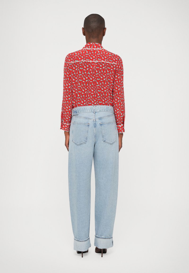 Camisa roja de manga larga con un pequeño patrón repetitivo, combinada con jeans de cintura alta de color azul claro con puños doblados y bolsillos traseros.