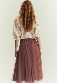 Krämfärgad blus med blommönster och volangärmar, ihopparad med en lång, lager-på-lager plommonfärgad tyllkjol med elastiskt midjeband.