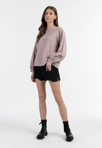 Lys rosa langærmet bluse med rund halsudskæring, parret med sorte slidte shorts og sorte snørestøvler. Glat stoftekstur.