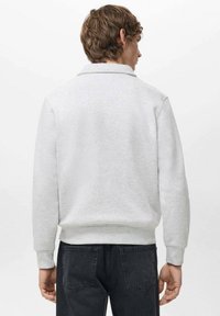 Jasnoszara bluza z kołnierzem, ściągaczami na rękawach i w pasie. Materiał wydaje się miękki; posiada prosty i czysty design bez ozdób.