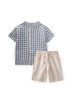 Kratka modro-bela srajca s kratkimi rokavi in gumbi, združena z bež kratkimi hlačami z elastičnim pasom, vrvico za zavezovanje in stranskimi žepi.