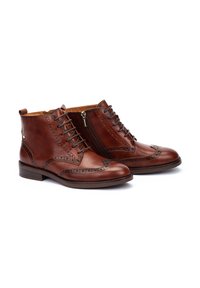 Bottines en cuir marron avec des détails brogués, fermeture lacée sur le devant et zip sur le côté ; texture lisse et bout rond, avec un talon plat.