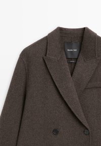 Brązowy płaszcz z wełny w połączeniu, z dwurzędowym zapięciem, kołnierzem z zakładkami i czarnymi guzikami, wykonany z miękkiego, teksturowanego materiału.