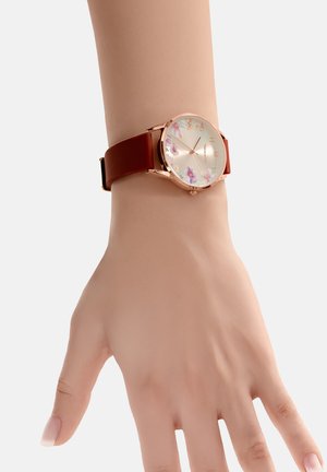 Pols met een roségouden bloemenhorloge met paarse en oranje bloemen en een bruine leren band op een lichte achtergrond.