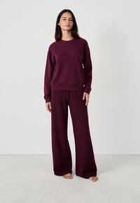 Burgundy sweatshirt och vida byxor-set, tillverkat av mjukt tyg. Sweatshirten har rund halsringning och ribbade ärmslut.