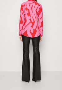 Camicia a maniche lunghe con un motivo astratto rosso e rosa, colletto con bottoni, abbinata a pantaloni in pelle neri a zampa d'elefante e tacchi alti.