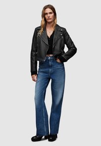 Giacca biker in pelle nera corta sopra una maglietta nera, abbinata a jeans blu a vita alta e gamba larga e scarpe con piattaforma nere.
