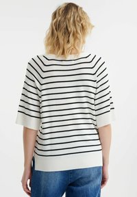 Gestreepte trui in crème en zwart, met korte mouwen, een relaxte pasvorm en een geribbelde zoom. Ontworpen met zijsplitten voor extra bewegingsvrijheid.