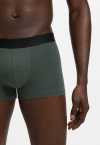 Dark green boxer shorts with a black textured waistband, fitted design, and soft fabric. Features a seamless leg opening for comfort.