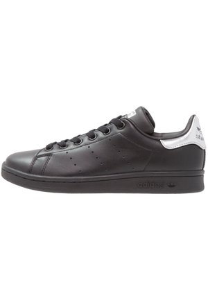 Niskie czarne skórzane sneakersy Adidas Stan Smith z czarnymi sznurowadłami i białą tylną częścią, widok z boku z detalem perforowanych pasków.