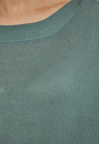 Tummansininen neulepaita, jossa on pyöreä kaula-aukko; rakenne on sileä ja löysä kudontamalli, joka korostaa keveyttä ja hengittävyyttä.