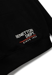 Černá mikina s kapucí, obsahující přední kapsu, pružné manžety a logo s textem "BENETTON DEPT." v bílé a červené barvě, založeno v roce 1965.