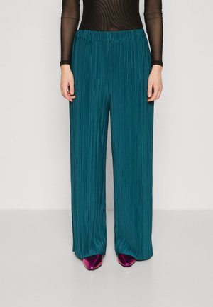 Teal plisserede bukser med brede ben og elastisk talje, lavet af tekstureret stof. Sammelt med skinnende fuchsia spidse sko.
