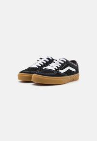 Sneakers negre din suede cu sireturi albe și o dungi albe pe lateral. Prezintă o talpă din cauciuc texturat de culoare caramel și cusături albe contrastante.