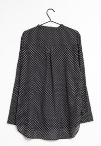 Svart långärmad skjorta med små vita hjärtan som hänger på en svart galge mot en vit bakgrund.