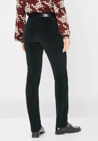 Zwarte corduroy broek met een fitted ontwerp, voorzien van achterzakken en een gladde textuur. Gecombineerd met glanzende zwarte loafers.