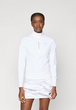 Balts garās piedurknes krekls ar rāvējslēdzēju, kura virsma ir maiga, apvienots ar vieglu, rakstainu svārku ar pelēkiem toņiem un mazu logotipa detaļu.