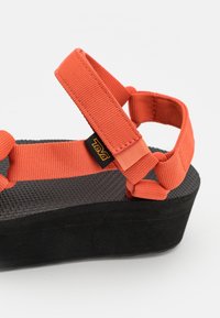 Tento sandál značky Teva se vyznačuje oranžovými nastavitelnými popruhy a texturovanou černou platformou, která má odolný design a polstrovanou podrážku.