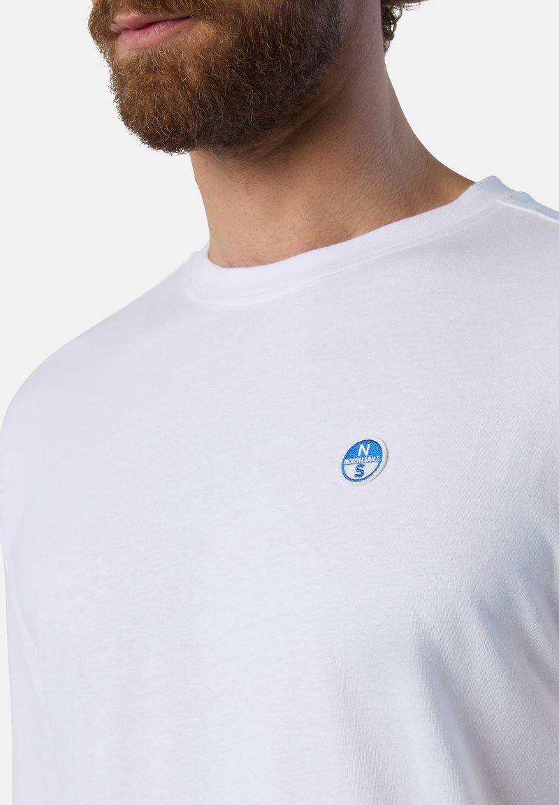 T-shirt bianca a girocollo realizzata in cotone, con un piccolo logo ricamato blu sul lato sinistro del petto. Tessuto morbido e vestibilità standard.