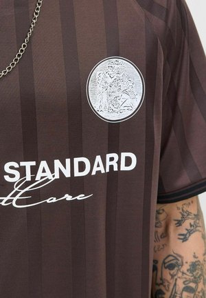 Brown striped jersey featuring a round silver logo on the chest, with white text reading "STANDARD" and "Core" below the logo.
