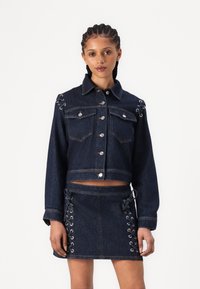 Denim jope hõbedaste nuppudega, kaks rinna taskut ja külgedel silmadega nöörimine. Kombineeritud sobiva mini-seelikuga, millel on nöörimisdetailid.